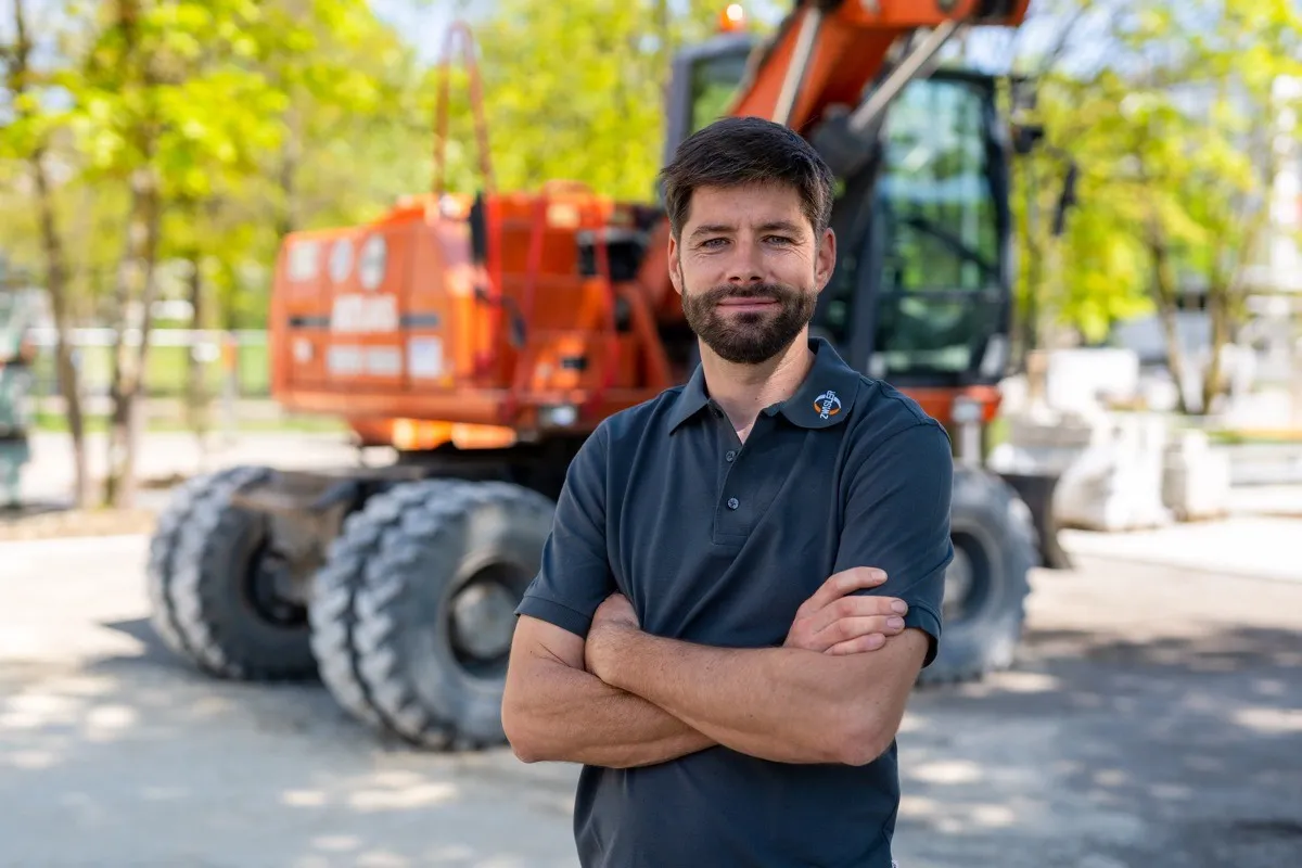 Bauarbeiter im Portrait vor einem gelben Bagger auf einer Baustelle